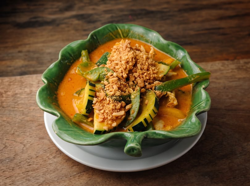 Red curry with zucchini, green beans, and crushed peanuts in a green leaf-shaped bowl.