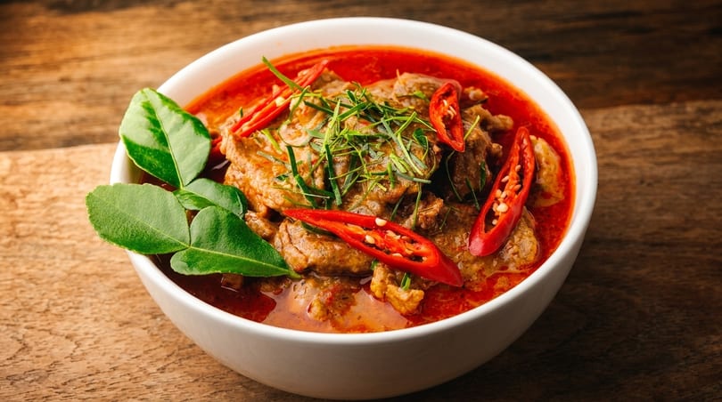 Red curry with beef, kaffir lime leaves, and sliced red chilies in a white bowl.
