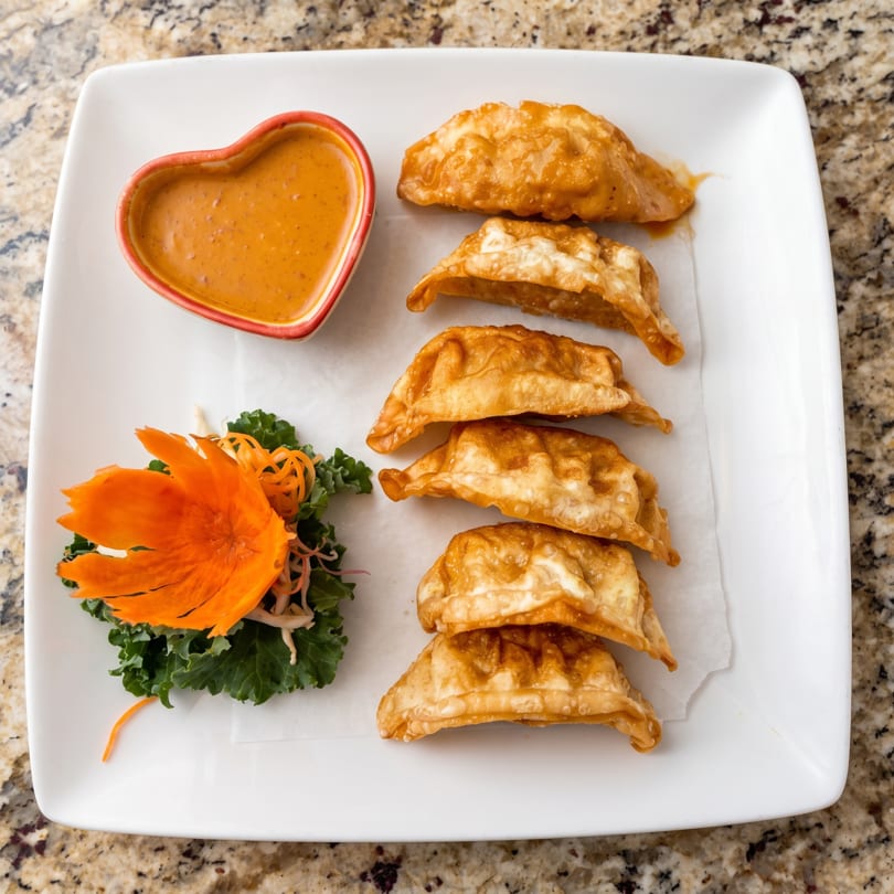 Fried dumplings with a heart-shaped dipping sauce bowl and a carved carrot garnish on a white plate.