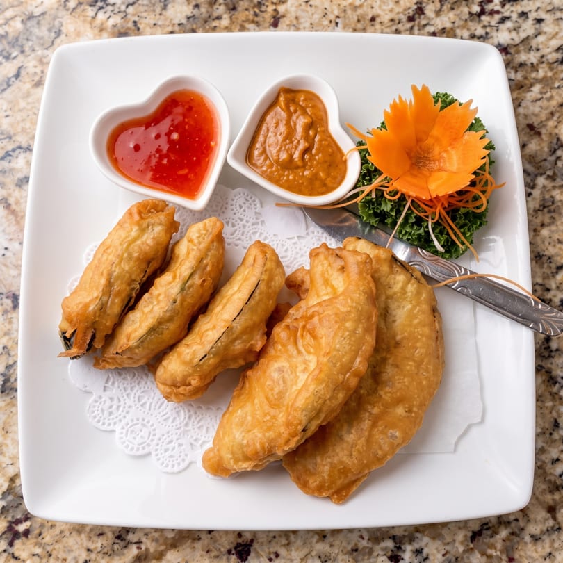 Crispy fried banana fritters with sweet chili and peanut sauces, garnished with a carrot flower.