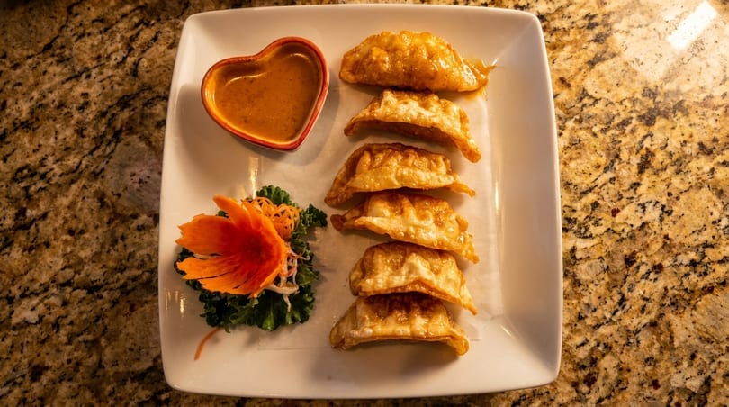 Six crispy fried dumplings with a heart-shaped sauce dish and garnish on a white plate.